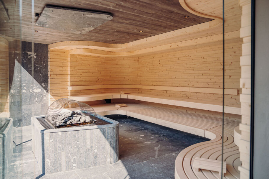 Bergsauna mit geschwungenen Holzbänken und Blick durch die Panoramafront