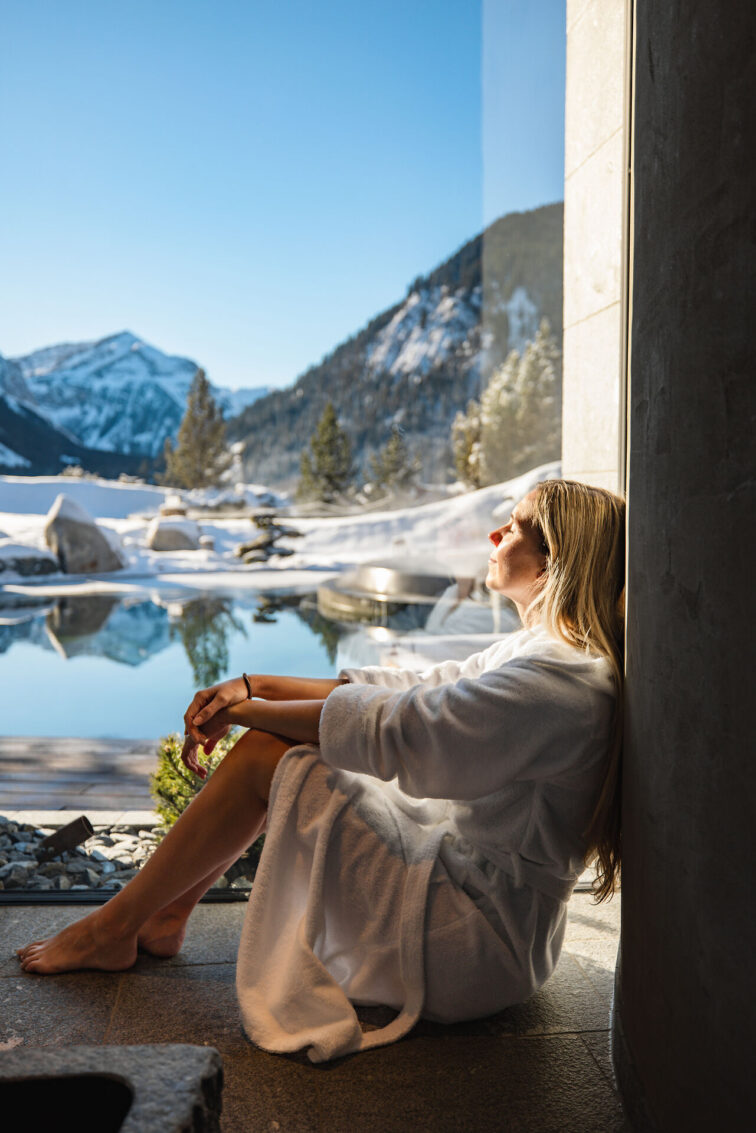 Frau im Wellnessbereich mit Blick über den Quellteich in die verschneite Bergwelt